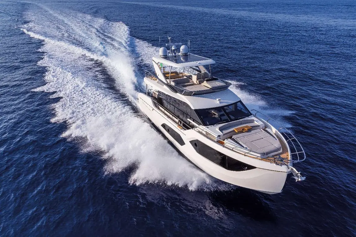 Luxury yacht cruising through deep blue waters, leaving a white frothy wake behind it under clear skies.